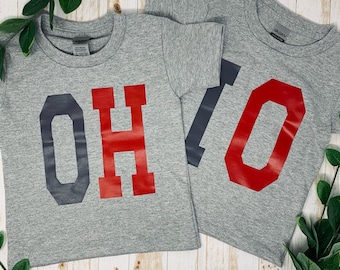 May include: Two gray t-shirts with the word "OHIO" printed in large, bold letters. The "O" is in dark gray, the "H" is in red, and the "I" is in dark gray.