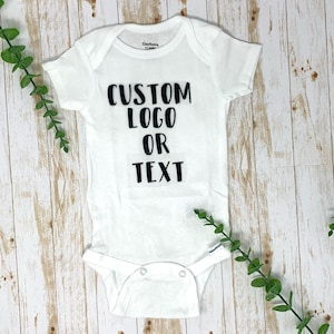 May include: White baby onesie with black text that reads "CUSTOM LOGO OR TEXT".