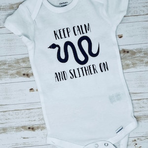 May include: White baby onesie with black text that reads "Keep Calm and Slither On" with a black snake graphic.