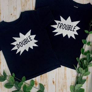 May include: Two black t-shirts with white text. One shirt says "Double Trouble" and the other says "Trouble".