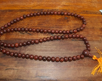 May include: A brown wooden mala bead necklace with a tassel. The beads are round and have a smooth finish. The tassel is made of yellow fabric.