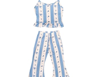 May include: A two-piece pajama set featuring a camisole top and flared pants. The set is patterned with vertical light blue stripes and small blue floral accents. The top has thin straps and a ruffled hem.