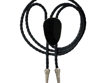 May include: A black bolo tie with a large, oval-shaped black stone pendant. The pendant is framed with a silver-colored trim. The braided black cord loops around and ends with decorative silver-colored tips.