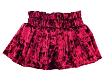 May include: A vibrant red velvet skirt with a gathered waistband. The skirt has a flared silhouette and a rich, textured appearance. The fabric has a crushed velvet effect, creating a play of light and shadow. This skirt is suitable for various occasions.