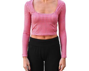May include: A long-sleeved crop top in a red and white gingham pattern. The top has a scoop neckline and is paired with black pants. The outfit is shown against a white background.