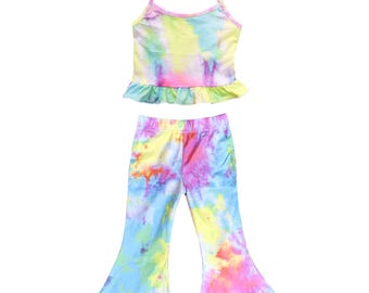 May include: A two-piece tie-dye outfit featuring a camisole top and flared pants. The top has thin straps and a ruffled hem. The pants have a wide leg. The colors include yellow, pink, blue, and purple.