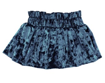 May include: A teal velvet skirt with a gathered waistband. The skirt has a flared silhouette and a soft, textured appearance. The fabric has a crushed velvet effect, creating variations in color and depth.