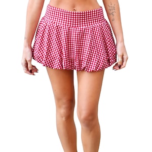 May include: A red and white gingham mini skirt. The skirt has a high waist and a flared, bubble-like shape. The fabric is a classic checkered pattern, with alternating red and white squares. The skirt is designed to be worn at the waist.