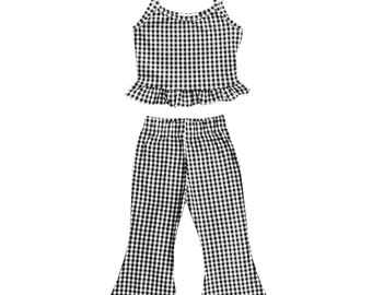 May include: A black and white gingham two-piece outfit. The top is a camisole with spaghetti straps and a ruffled hem. The pants are flared at the bottom. The outfit is made of a lightweight fabric.