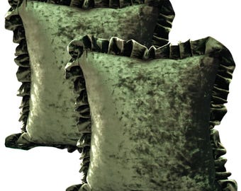 May include: Two sage green velvet throw pillows with ruffled edges. The pillows have a soft, textured appearance and a square shape. The ruffled trim adds a decorative element to the pillows, which are suitable for home decor.