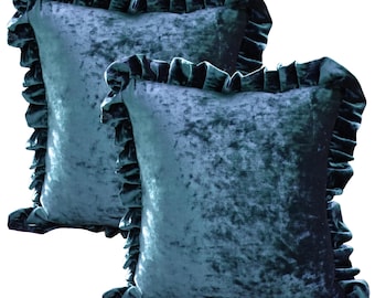 May include: Two teal velvet throw pillows with ruffled edges. The pillows have a soft, crushed velvet texture and a square shape. The ruffled trim adds a decorative element to the pillows, which are suitable for a bed or sofa.