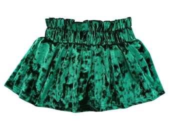 May include: A vibrant green velvet skirt with a gathered waistband. The skirt has a flared silhouette and a soft, textured appearance. The fabric has a crushed velvet effect, creating a play of light and shadow.