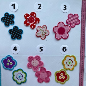 Könnte beinhalten: Eine Sammlung bunter, blütenförmiger Stoffaufnäher. Die Aufnäher weisen verschiedene Muster auf, darunter Punkte, Vichy-Karo und Blumendrucke. Die Farbpalette umfasst Rot, Rosa, Blau, Grün und Weiß. Diese dekorativen Aufnäher eignen sich ideal für Bastelarbeiten und Verzierungen.