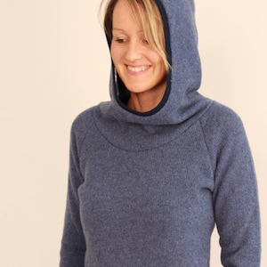 May include: A blue hooded sweater with a high collar and a small embroidered detail on the hood. The sweater has long sleeves and a comfortable, relaxed fit. The hood is lined with a darker blue fabric.