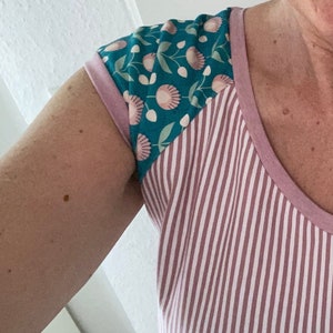 May include: A pink and white striped shirt with a teal floral pattern on the sleeves. The shirt has a v-neck.