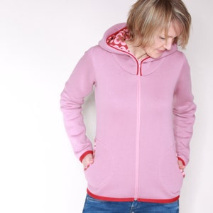 May include: A pink hooded sweatshirt with red trim and a zip fastening. The hood is lined with a floral pattern.