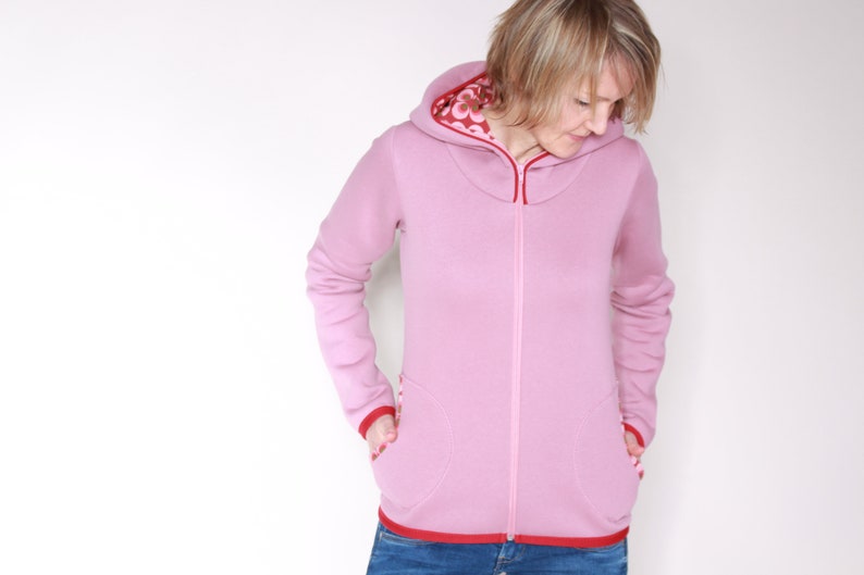 May include: A pink hooded sweatshirt with red trim and a zip fastening. The hood is lined with a floral pattern.