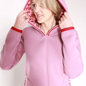May include: A pink hooded sweatshirt with a red zip and red trim. The hood is lined with a floral print fabric.