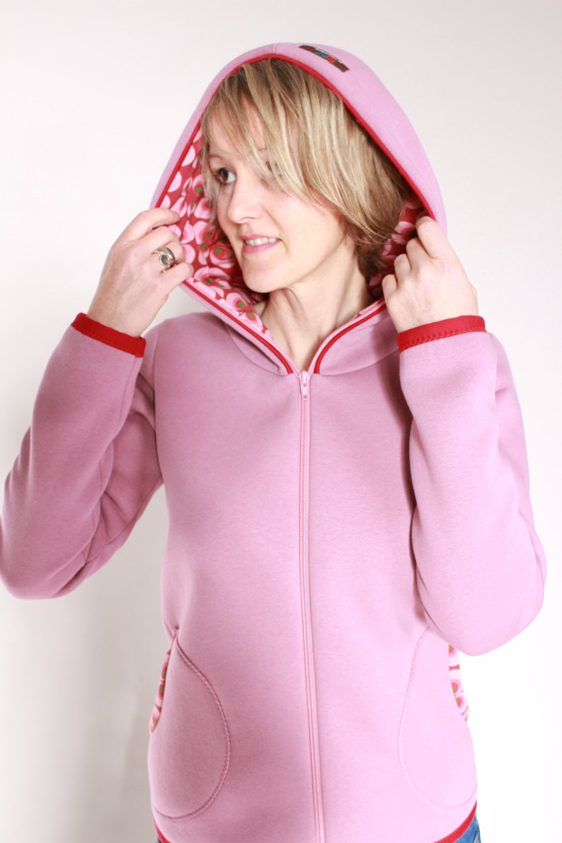 May include: A pink hooded sweatshirt with a red zip and red trim. The hood is lined with a floral print fabric.