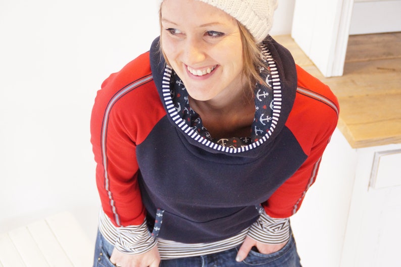 May include: A navy blue and red hooded sweatshirt with white trim and a white and blue anchor print lining the hood. The sweatshirt has a zipper detail on the sleeves.