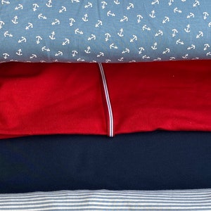 May include: Four different fabric swatches stacked on top of each other. The top swatch is a light blue fabric with a white anchor pattern. The second swatch is a solid red fabric. The third swatch is a solid dark blue fabric. The bottom swatch is a white and light blue striped fabric.