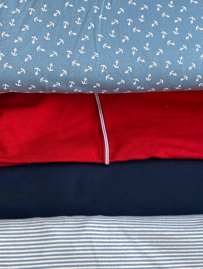 May include: Four different fabric swatches stacked on top of each other. The top swatch is a light blue fabric with a white anchor pattern. The second swatch is a solid red fabric. The third swatch is a solid dark blue fabric. The bottom swatch is a white and light blue striped fabric.