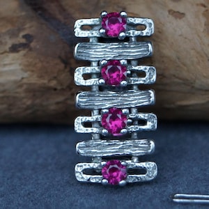 Könnte beinhalten: Ein silberner Anhänger mit geometrischem Design und vier rosafarbenen Edelsteinen.