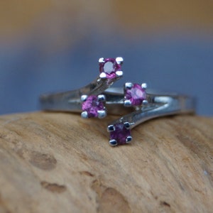 Könnte beinhalten: Ein silberner Ring mit vier rosafarbenen Edelsteinen, die in einem verdrehten Band gefasst sind.