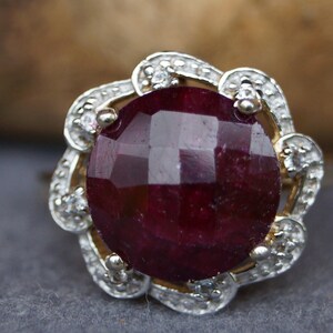 Könnte beinhalten: Ein Ring mit einem roten Edelstein und einem floralen Design. Der Ring ist in Gold gefasst und hat kleine Diamanten um den Edelstein.