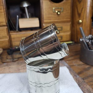 May include: Two silver bracelets with a wavy, textured design. The bracelets are stacked on top of each other.