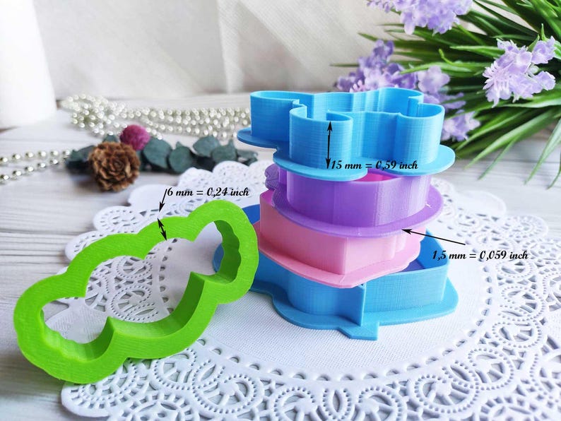 May include: A collection of plastic cookie cutters in various colours: blue, purple, pink, and green. The blue cutter is 15 mm (0.59 inches) tall, the green cutter is 6 mm (0.24 inches) wide, and the pink cutter is 1.5 mm (0.059 inches) tall.