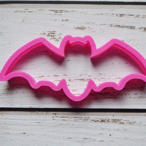 Puede incluir: Cortador de galletas rosa brillante con forma de murciélago. El cortador está hecho de un material sólido y tiene un diseño simple y limpio. El murciélago tiene alas extendidas y una cabeza detallada. Perfecto para hornear con temática de Halloween.