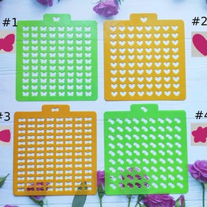 Puede incluir: Cuatro plantillas de plástico verde y naranja con diferentes formas. Las plantillas están numeradas del 1 al 4. La plantilla n.º 1 tiene forma de mariposa, la n.º 2 tiene forma de corazón, la n.º 3 tiene forma de lazo y la n.º 4 tiene forma de estrella.