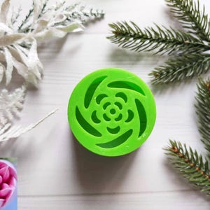May include: A green plastic mold for making a swirl rose design. The mold has a circular shape with a flower-shaped cutout in the center.
