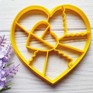 Puede incluir: Un cortador de galletas de plástico amarillo en forma de corazón con varios diseños en el interior, incluyendo un corazón más pequeño, líneas onduladas y un borde festoneado.