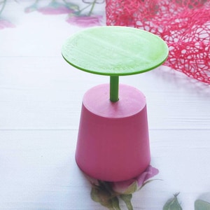 May include: A small, pink and green table with a round top. The table is made of plastic and has a simple design.