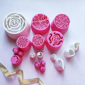 Könnte beinhalten: Eine Sammlung verschiedener Spritztüllen zum Verzieren von Torten in Rosa- und Weißtönen. Das Set enthält große, mittlere und kleine Tüllen mit komplizierten Ausschnittmustern zum Erstellen von Blumen- und Dekorationsformen auf Gebäck.
