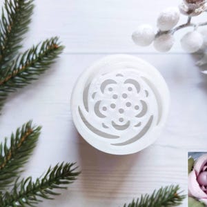 May include: White plastic mold for making a flower-shaped cake decoration. The mold has a detailed design of a rose with a swirl pattern. A pink rose made with the mold is shown in the lower right corner of the image.