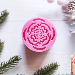 May include: Pink silicone mold with a detailed floral design. The mold is round and has a raised edge. The floral design is intricate and detailed, with a central flower surrounded by smaller flowers.