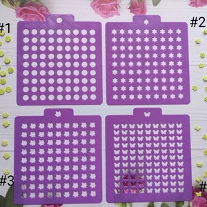 Peut inclure: Quatre pochoirs violets avec différents motifs : des cercles, des étoiles, des fleurs et des papillons. Chaque pochoir est numéroté de 1 à 4.