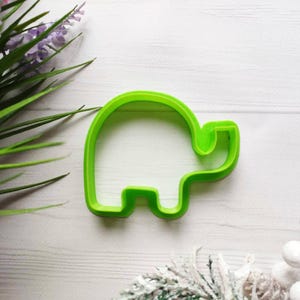 May include: Green plastic cookie cutter shaped like an elephant. The cutter is on a white wooden surface.
