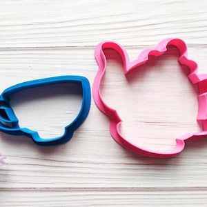 Könnte beinhalten: Zwei Ausstecher aus Kunststoff, einer in Form einer Teekanne und der andere in Form einer Teetasse. Der Teekannen-Ausstecher ist rosa und der Teetassen-Ausstecher ist blau.