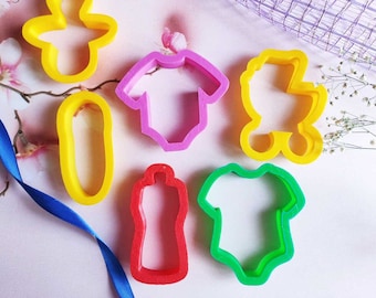 A set of children cookie cutters a pacifier, a safety pin, a bottle, a stroller, a body.
