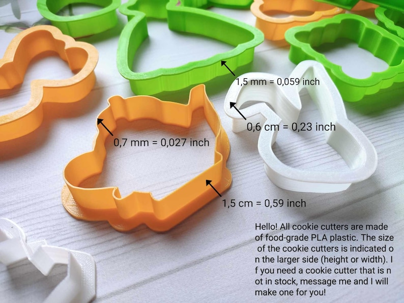 May include: A selection of colourful cookie cutters in orange, green, and white. The image shows the dimensions of the cutters in millimetres and centimetres. The text in the image says, "Hello! All cookie cutters are made of food-grade PLA plastic."