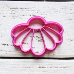 Puede incluir: Un cortador de galletas de plástico rosa en forma de concha. El cortador tiene un diseño detallado con múltiples crestas.