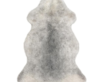 Puede incluir: Una alfombra de piel de oveja en tonos grises y blancos, con un aspecto suave y texturizado. La alfombra tiene una forma irregular, que se asemeja a la forma natural de la piel del animal. La variación de color crea un patrón sutil y orgánico, adecuado para la decoración del hogar.