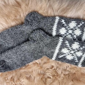 K&ouml;nnte beinhalten: Ein Paar graue Wollsocken mit wei&szlig;en Schneeflockenmustern. Die Socken sind gestrickt und haben eine flauschige Textur.