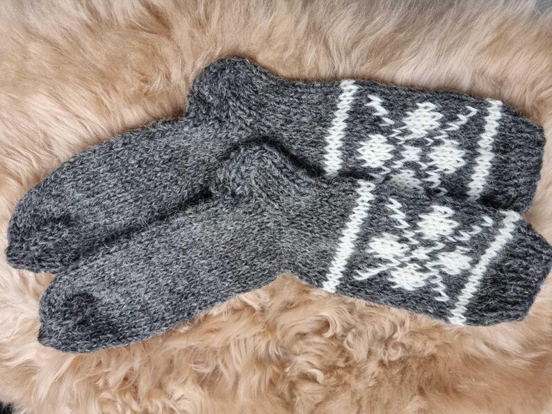 K&ouml;nnte beinhalten: Ein Paar graue Wollsocken mit wei&szlig;en Schneeflockenmustern. Die Socken sind gestrickt und haben eine flauschige Textur.