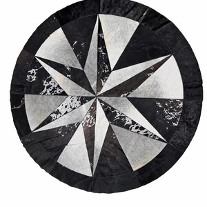Puede incluir: Una alfombra circular hecha de parches de piel de vaca en un patrón de estrella. El diseño presenta segmentos alternos de negro sólido, blanco y piel moteada en blanco y negro, todo encerrado dentro de un borde circular negro sólido.