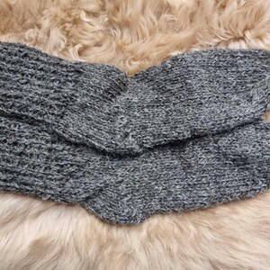 K&ouml;nnte beinhalten: Ein Paar graue Stricksocken mit einer flauschigen Textur. Die Socken sind in der H&auml;lfte gefaltet und auf einer flauschigen, hellbraunen Oberfl&auml;che ausgelegt.